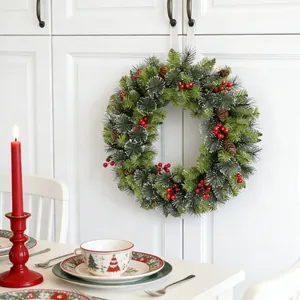 Festive Christmas wreath with red berries and pine cones hung on a white door
