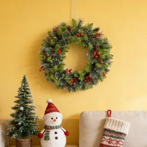 Lush artificial Christmas wreath with red berries and pine cones on yellow wall