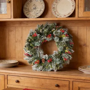 Nahaufnahme eines verschneiten Weihnachtskranzes mit Beeren und Lichtern auf Holz