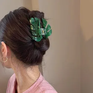 Detailed view of an elegant green Monstera leaf acetate hair claw clip styled in dark hair.