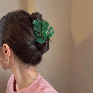 A stylish green leaf-shaped acetate hair claw clip shown in an updo on a female model