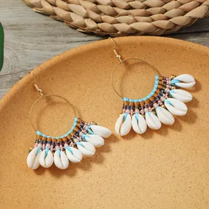 Λεπτομέρεια από χειροποίητα boho σκουλαρίκια με πλεκτή ύφανση και φυσικά κοχύλια κάουρι.