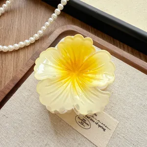 Close-up of a gradient yellow flower hair claw clip on a natural wooden background.