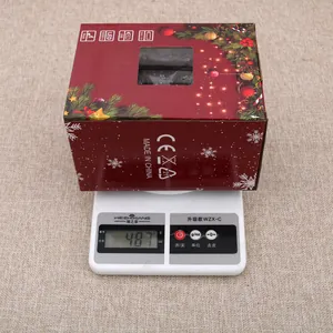 Christmas musical snowing house lantern in festive red box being weighed on a scale