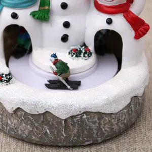 Close-up of a rotating Christmas snowman music box featuring a miniature skier figurine gift