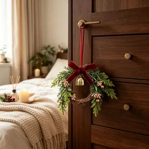 Kleine kerstkrans met dennenappels en een gouden bel hangend aan een houten ladekast