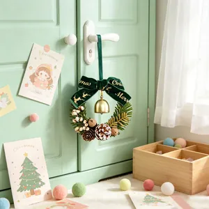 Mini kerstkrans met dennenappels en groene fluwelen strik opgehangen aan een muntgroene deur
