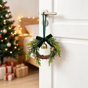 Kleine feston-kerstkrans voor de deur met groene strik, gouden bel en dennennaalden
