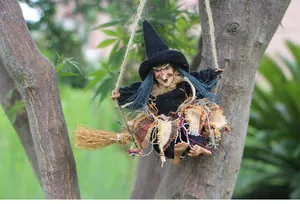Vista detallada de una muñeca de bruja de Halloween colgada de una escoba de madera.