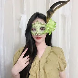 Nahaufnahme einer eleganten grünen Spitzenmaske mit Blumen- und Federakzenten
