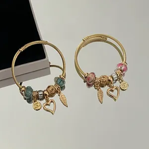 Gold-plated wire bracelet with heart and feather charms and colorful DIY beads.