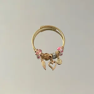 Detailed view of gold beaded wire bracelet with heart and angel wing charms.