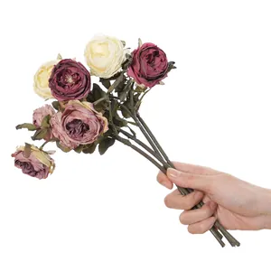 Detailed macro view of a hand holding vintage autumn style artificial rose flower bouquet