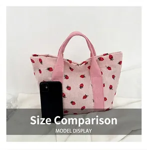 Size comparison of the pink strawberry print corduroy tote bag with a black smartphone