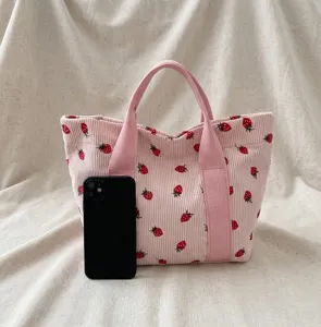 Groottevergelijking van de roze corduroy draagtas met aardbeien en een zwarte smartphone