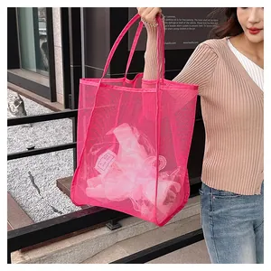 Female model carrying a large vibrant pink mesh beach bag for travel and storage
