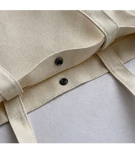 Close-up detail of metal snap button closure on durable cream canvas tote bag