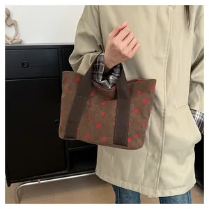 Detail shot of a brown corduroy tote bag with strawberry prints held by a model.