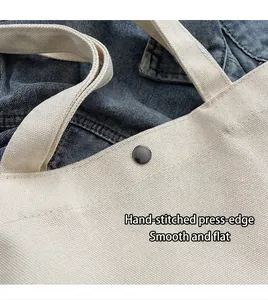 Detail shot showing hand-stitched edge and metal snap button of the white canvas tote bag.