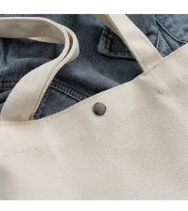 Detailaufnahme der handgenähten Kante und des Metalldruckknopfs der weißen Canvas-Tasche.