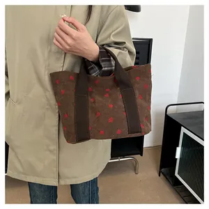 Detail of a corduroy tote bag with strawberry patterns held by a person in a coat.