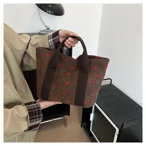 Detail view of a brown corduroy tote bag with red strawberry prints held by a person.