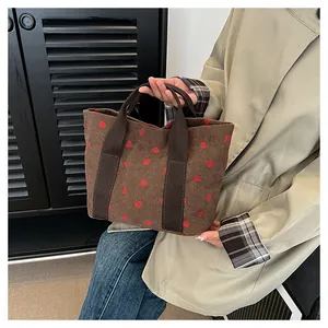 Detailed close-up of a brown corduroy tote bag with strawberry prints held by a fashion model.