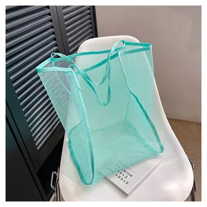 Large turquoise mesh beach storage bag displayed on a stylish white chair with book prop.