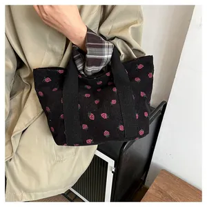 Detailed view of a black corduroy tote bag featuring a cute pink strawberry print.