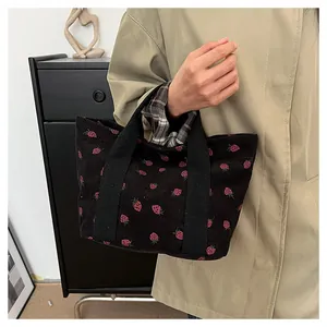Close-up detail of a black corduroy tote bag with strawberry print carried by a model