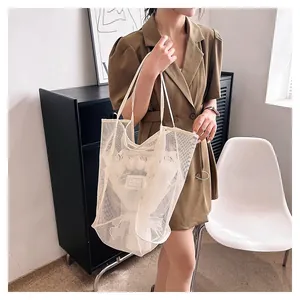 Detail view of a large white mesh tote bag held by a model in a stylish indoor setting