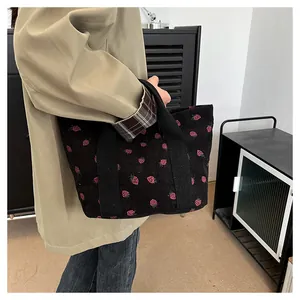 Detailed side view of a black corduroy tote bag with cute pink strawberry prints.