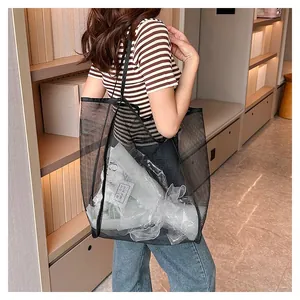 Large capacity black mesh travel storage bag used by a model in a modern interior setting
