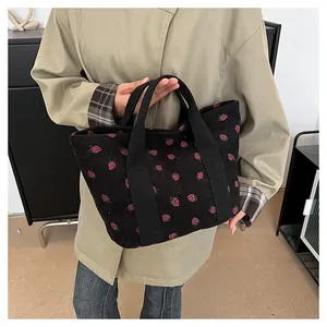 Black corduroy tote bag featuring red strawberry print pattern held by a model