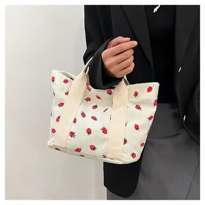Close-up of a corduroy tote bag with strawberry print held by a person in a black blazer.