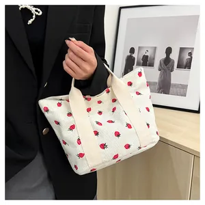 Close-up detail of corduroy tote bag with cute strawberry print pattern held by hand.