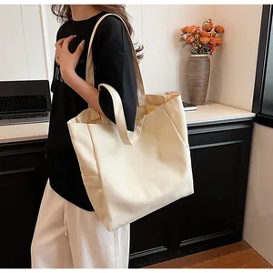 Detailed view of a minimalist cream canvas tote bag worn on shoulder in a modern room setting.