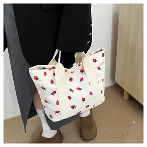 Close-up detail view of a corduroy tote bag with cute strawberry prints held by a person.