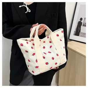 Detailed lifestyle shot of a white corduroy tote bag featuring a cute red strawberry print