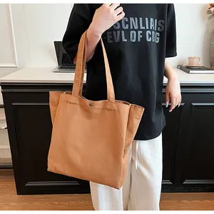 Detail of a camel canvas tote bag held by a model in a casual indoor setting