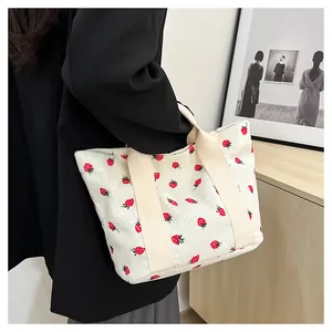 Close-up of a white corduroy tote bag with strawberry prints being carried by a model.
