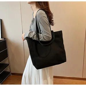Minimalist black canvas tote bag shown on model in a modern indoor lifestyle setting