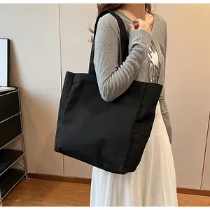 Detailed view of a minimalist large black canvas tote bag carried by a model in lifestyle setting