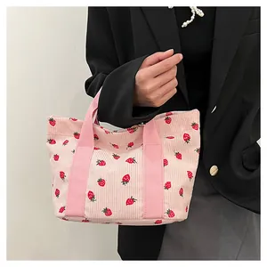 Detailed view of a pink corduroy tote bag featuring cute red strawberry patterns.