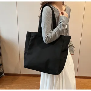 Side view detail of a minimalist black canvas tote bag carried by a model on shoulder