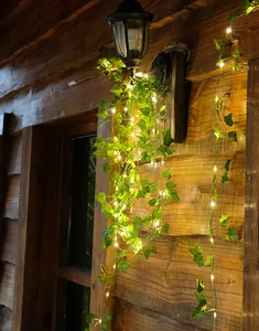 Warme LED-Lichterkette mit künstlichen grünen Efeublättern an einer rustikalen Holzwand