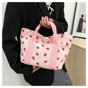 Close-up of a stylish pink corduroy tote bag with strawberry print being held by a hand