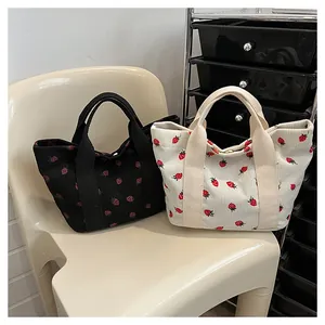 Detail view of corduroy tote bags with cute strawberry prints in black and cream.
