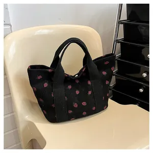 Close-up of black corduroy tote bag featuring vibrant red strawberry print pattern.