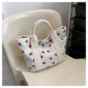 Detail view of a white corduroy tote bag with a cute red strawberry print pattern.
